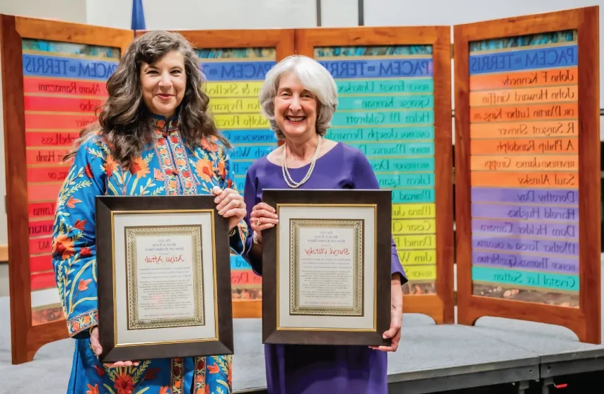 Two women holding up awards and smiling.